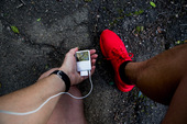 一个男人跑着，从个人的角度检查他的mp3耳机和穿着红色运动鞋在柏油路上。图片素材