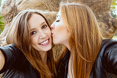 年轻女子在自拍，而她的女性朋友亲吻她的脸颊图片素材