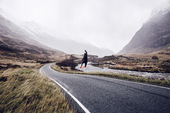 一位自由奔跑者在苏格兰公路上高兴地跳着。图片素材