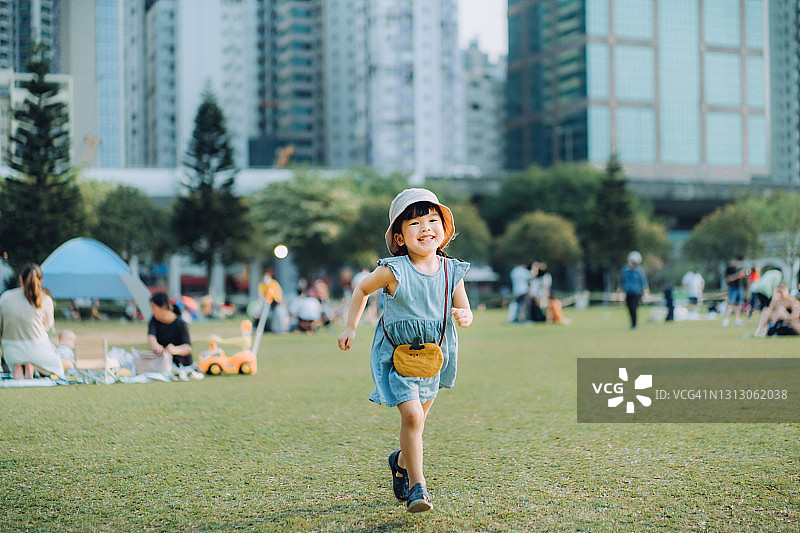 快乐的小亚洲女孩在城市公园里跑来跑去，快乐地微笑着。享受自由和自然之美。以现代城市景观为背景图片素材