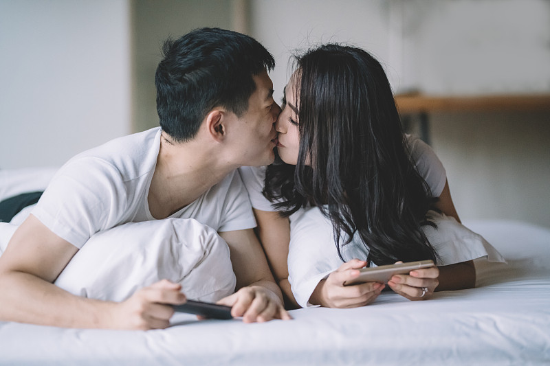 一對亞洲華人夫婦躺在床上玩手機游戲，早上玩得很開心圖片下載