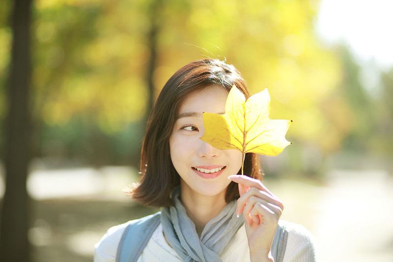 在秋天的公園里，年輕女子抱著一片樹葉圖片素材