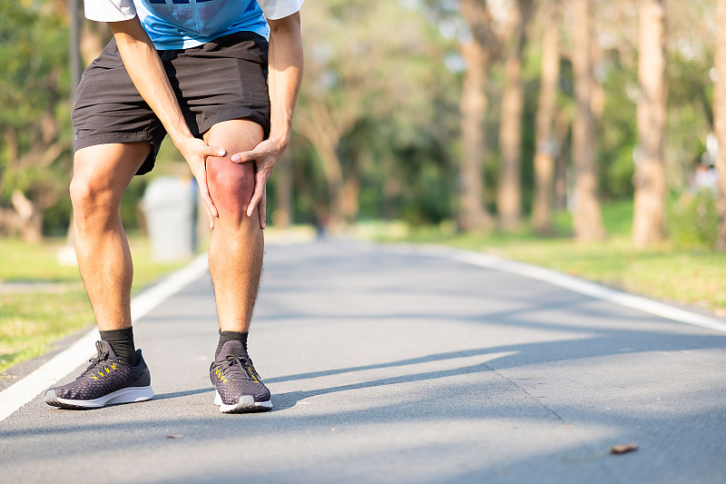 男人站在路上疼痛地觸摸膝蓋的低部位圖片素材