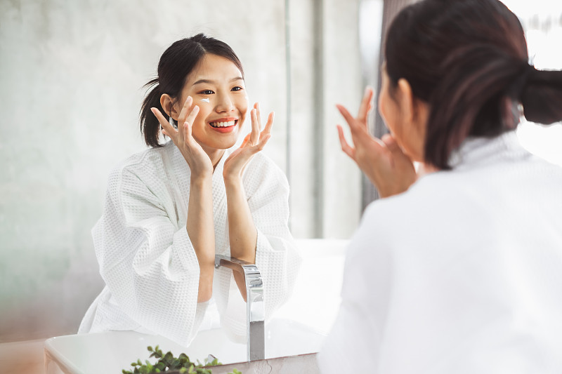 一名年輕女子微笑著在浴室鏡子上擦潤膚霜圖片素材