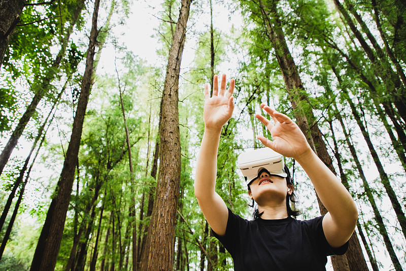 一個女人在森林中使用虛擬現實頭盔圖片素材