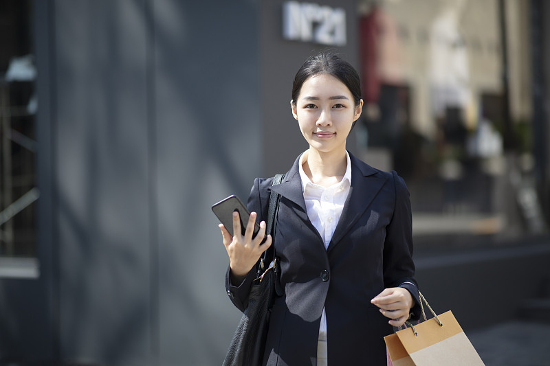 一名年輕女子在戶外拿著智能手機拎著購物袋圖片素材