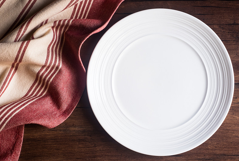 在舊的木制棕色背景上，空的餐巾白色盤子，俯視圖。圖像與復制空間。廚房桌子與毛巾和一個盤頂視圖與復印空間。圖片素材