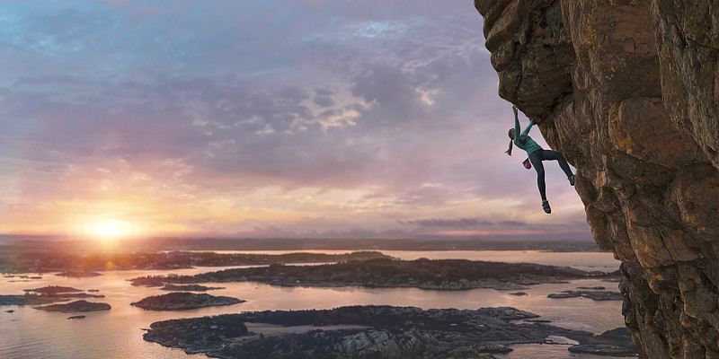 女性自由攀登者在黎明攀登陡峭的海岸巖石面圖片素材