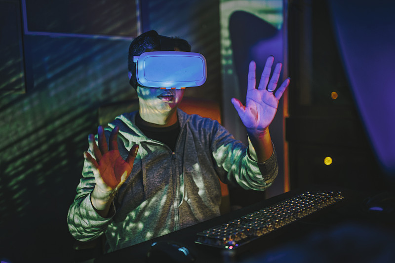 an asian chinese male put on VR goggle and experiencing 3D virtual gaming experience in his home office study room at night in front of his desktop PC圖片素材