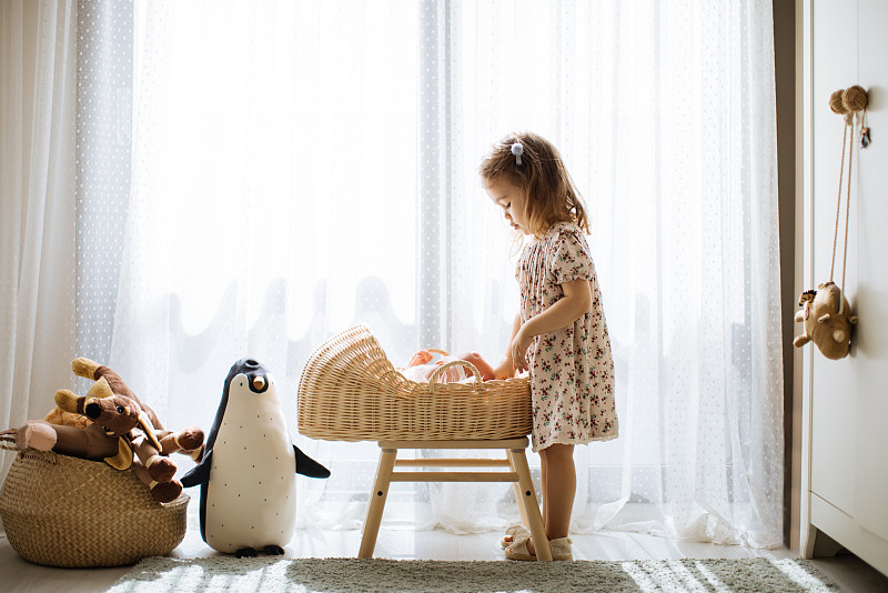 可愛的小女孩在嬰兒床里喂她的玩具娃娃，在有大窗戶的陽光臥室里玩圖片素材