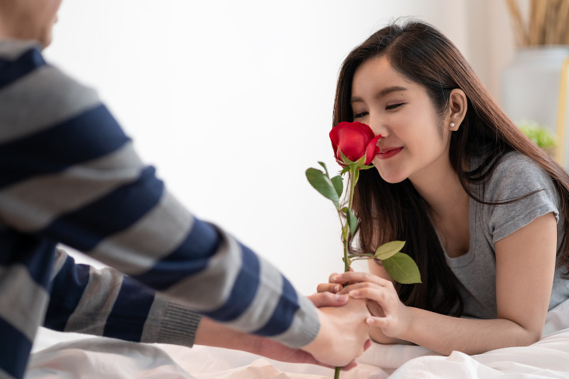 浪漫的亞洲夫婦在臥室，一個男人給美麗的女人一朵玫瑰，同時親吻美麗的玫瑰，充滿愛和幸福。美麗優雅的亞洲夫婦在臥室擁抱和微笑圖片下載