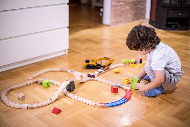 漂亮的小男孩在玩火車玩具和塑料交通工具。圖片素材