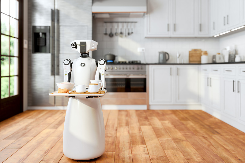 在模糊背景的現代家庭廚房里，機器人女傭端著盤子，端著食物和飲料。人工智能和智能機器人概念。圖片素材