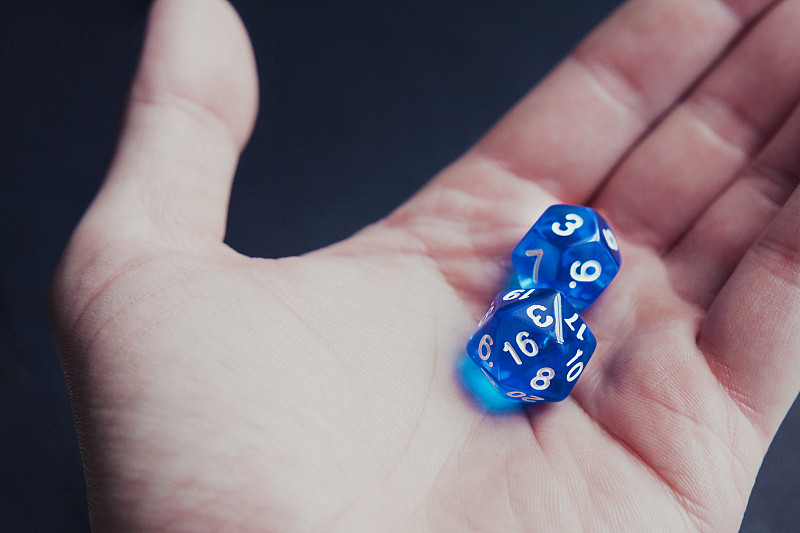 男人的手握兩個藍色的多面體骰子設置在黑暗的背景。攝影圖片