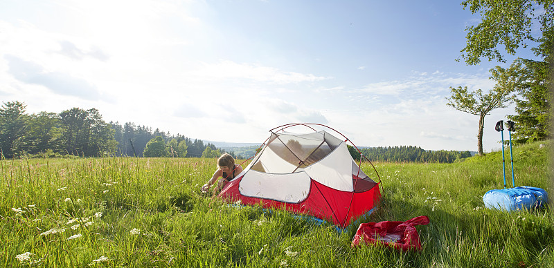 在陽光明媚的日子里，孤獨的女性在茂盛的草地上搭帳篷攝影圖片