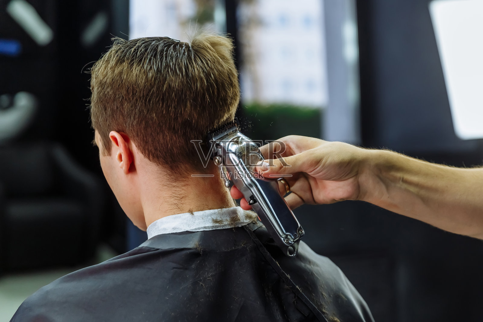 男性用电动剃须刀理发。理发师在理发店用理发器为顾客理发。男人用电动剃须刀理发照片摄影图片