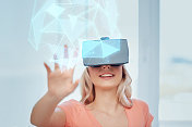 技术，增强现实，网络空间和人的概念-快乐的年轻女子戴着耳机或3d眼镜在家里玩游戏看虚拟投影的低多边形形状图片素材