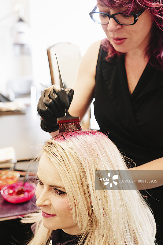 染发师戴着手套，用刷子将红色染发剂涂在客户的金发上。图片素材