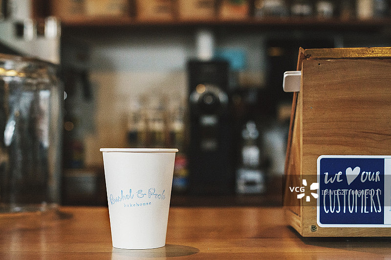 一个印有咖啡店名称的纸杯，柜台上有一个标志。图片素材