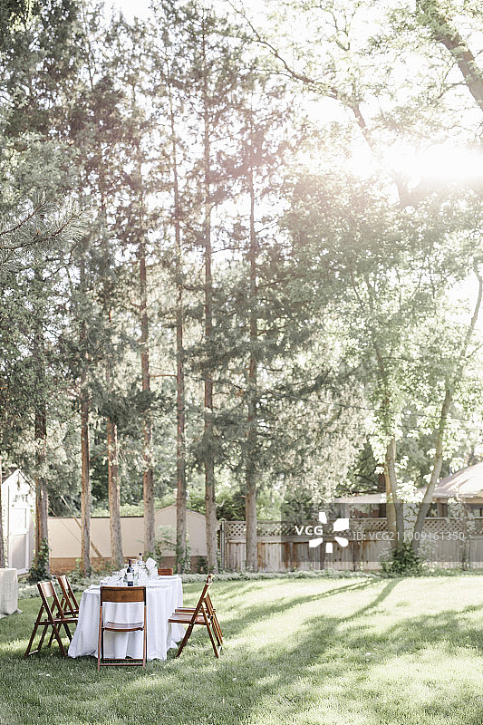 在花园里用白色桌布和木椅布置餐桌。图片素材