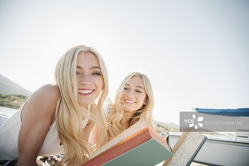 两个金发姐妹躺在码头上，在读一本书。图片素材
