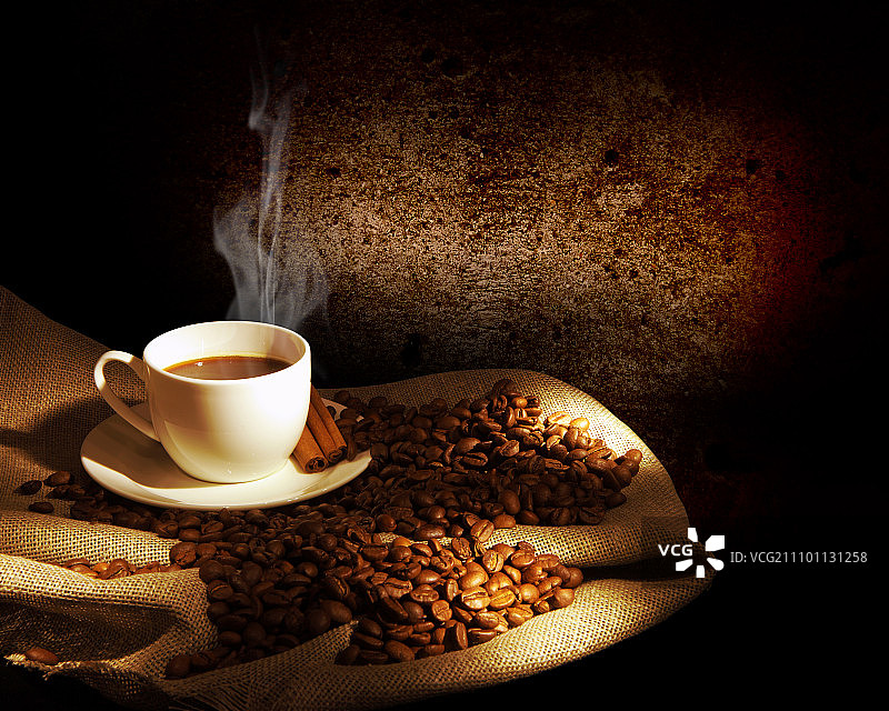 一杯热气腾腾的咖啡，肉桂棒和一些咖啡豆。静物画图片素材