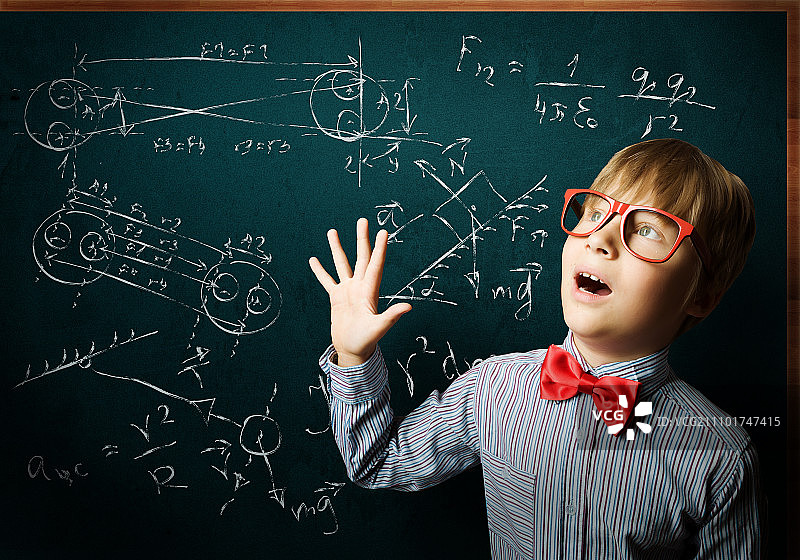 聪明的学生。戴着红眼镜的天才男孩在黑板旁边写着公式图片素材