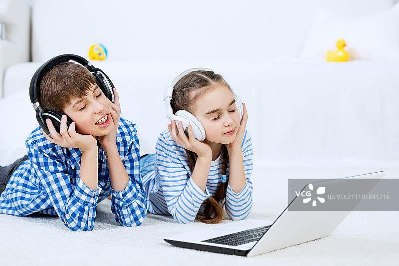 可爱的孩子使用设备。男孩和女孩躺在地板上使用笔记本电脑图片素材