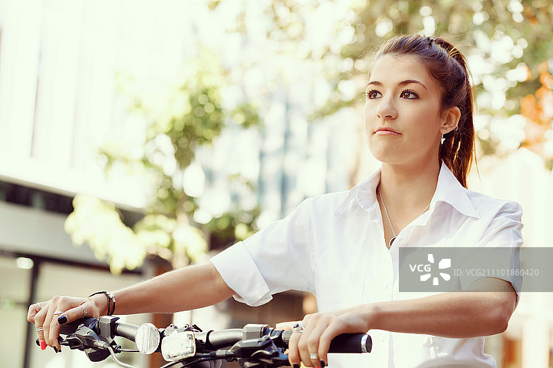 快乐的年轻女自行车手的肖像。肖像的快乐年轻女自行车骑在城市图片素材