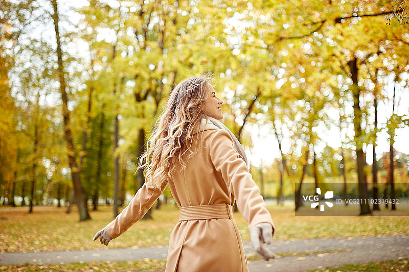 季节与人的概念——美丽快乐的年轻女子漫步在秋天的公园里。美丽快乐的年轻女子漫步在秋天的公园图片素材
