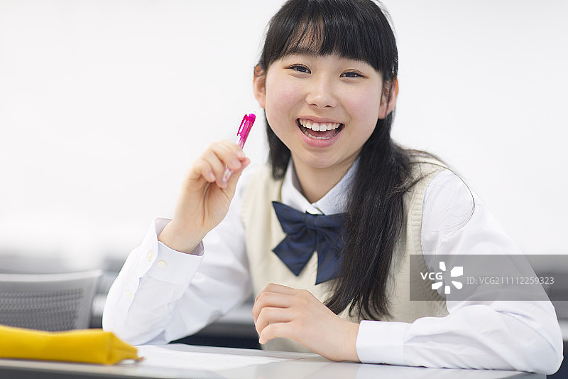 女学生微笑着用钢笔在教室里图片素材