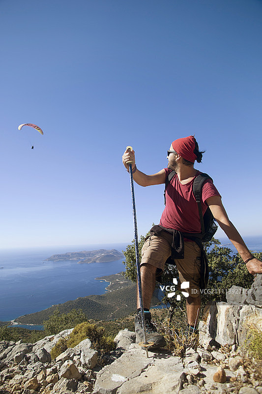 一位男性登山者在土耳其安塔利亚的卡斯山徒步旅行时看着滑翔伞图片素材
