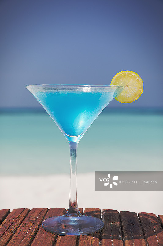 阳光明媚的热带海滩上的蓝色鸡尾酒和柠檬片马提尼杯图片素材