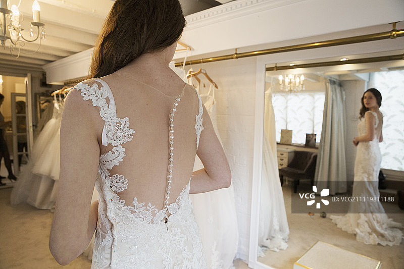 在一家婚礼精品店里，一位穿着白色婚纱的年轻女子看着镜子里自己的倒影。图片素材
