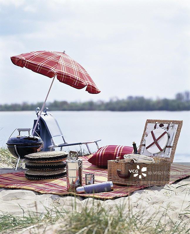 湖边野餐毯上放有野餐用品、野餐篮、雨伞等图片素材