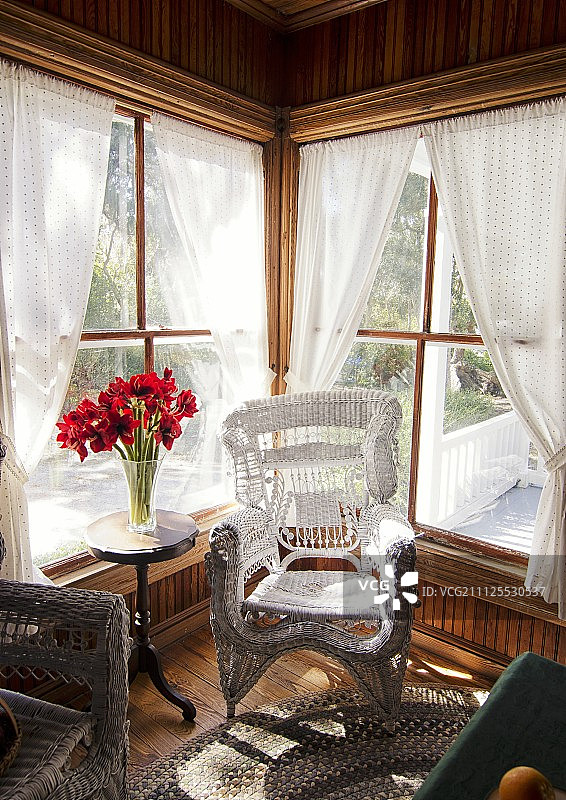 窗边的白色柳条椅;桌上的花瓶里插着红花图片素材