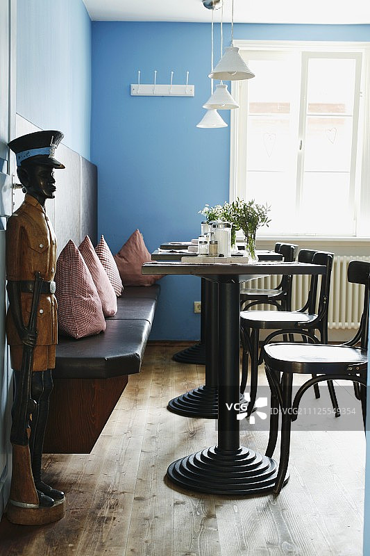餐厅里有小酒馆的桌子，木凳上有靠垫，蓝色的墙壁和木制的男人雕塑旁边开着门图片素材