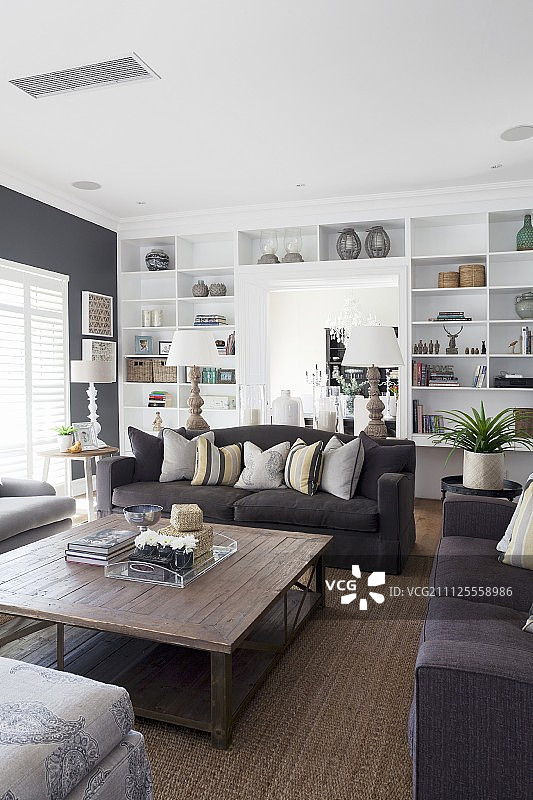 客厅的木桌周围摆放着黑色沙发，背景是白色的置物架图片素材