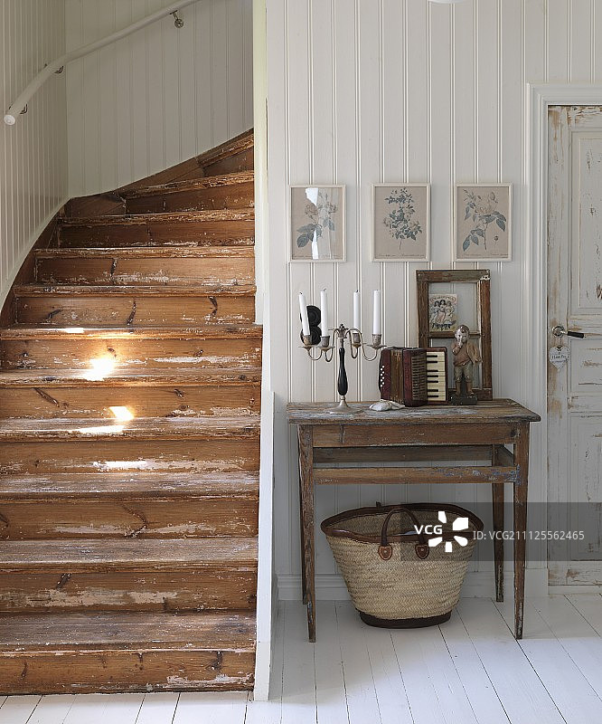 白色木墙边，简单的桌子上放着烛台和老式手风琴;一边是质朴的木制楼梯图片素材