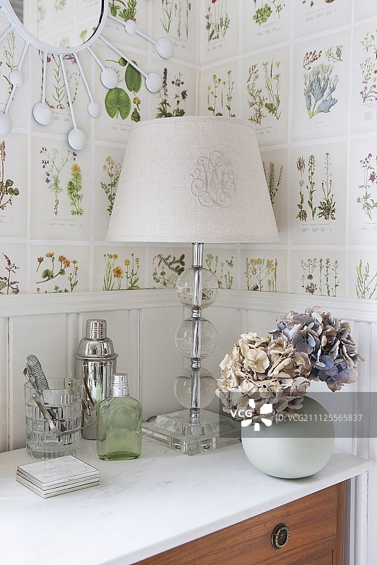 带有白色灯罩和绣球花球形花瓶的台灯，贴着植物墙纸放在五斗橱上图片素材