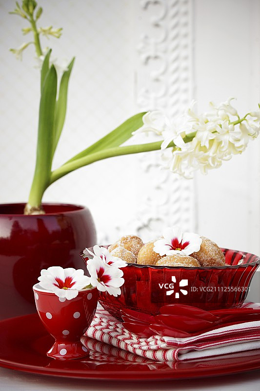 小甜甜圈放在红色玻璃碗里，桌子上装饰着报春花和风信子图片素材