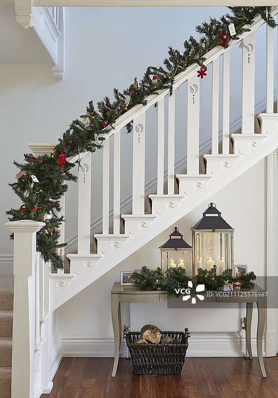 用杉木树枝装饰的白色木制楼梯，以及弯曲腿的控制台桌上的灯笼上面的圣诞装饰品图片素材