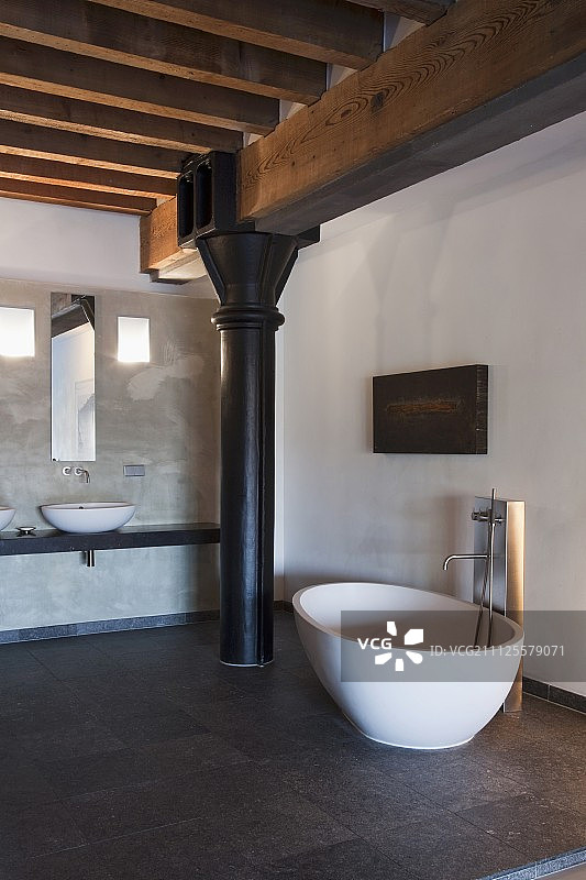 独立的设计师浴缸，在黑色金属柱前的石头瓷砖地板上安装水龙头图片素材