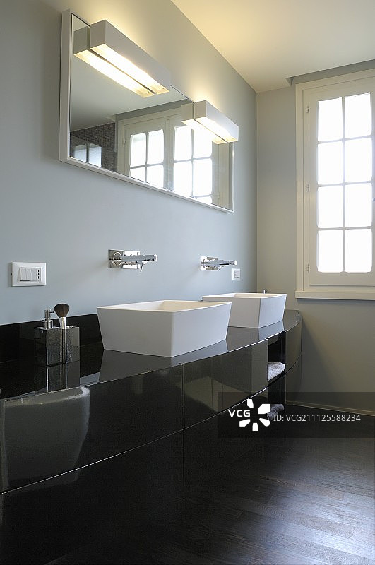 黑色的弯曲盥洗台，配有白色的洗手盆，在灰色墙壁上的镜子下面安装在墙上的水龙头图片素材