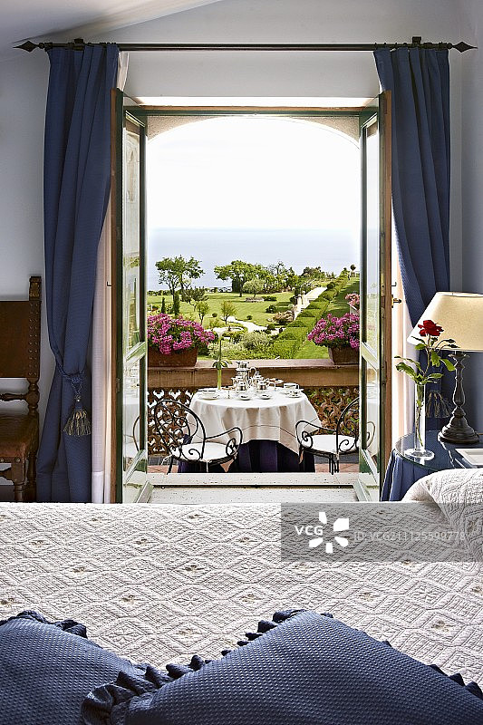 酒店客房，通过开放式阳台门可以看到餐桌、公园和海洋(意大利Cimbrone别墅酒店)图片素材