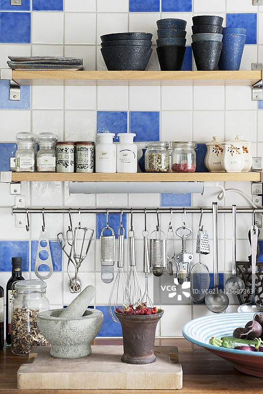 厨房墙上的不锈钢杆上挂着香料和餐具架，上面铺着白色和蓝色瓷砖图片素材