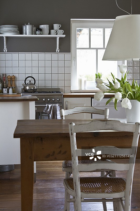 现代厨房中白色吊灯下的旧木桌，白色柜台映衬着灰色的墙壁图片素材