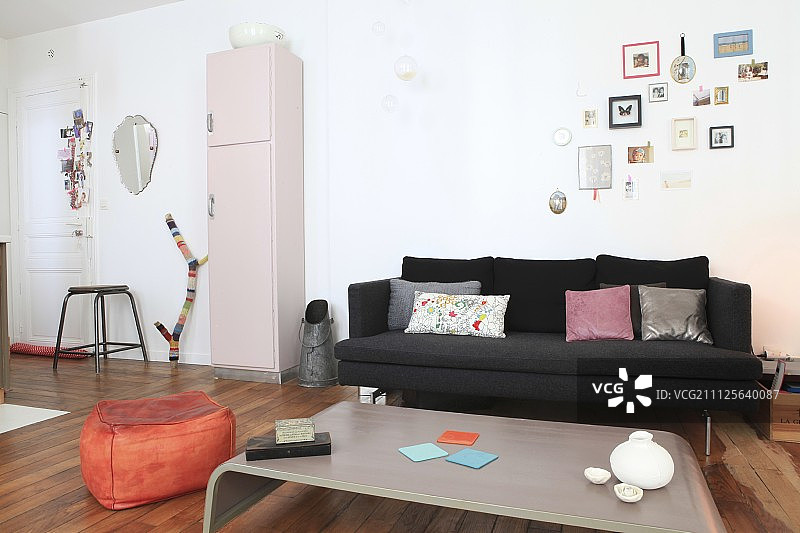 开放式起居区的黑色沙发、煤斗、粉色复古橱柜和橙色坐垫图片素材