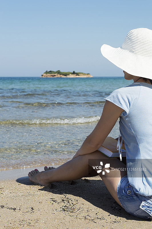 一个女人坐在海滩上拿着一本书图片素材