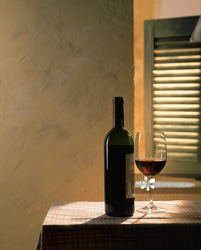 窗前的桌子上放着酒瓶和玻璃杯里的红酒图片素材